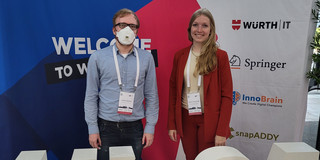 Björn Konopka und Amelie Schmidt vor WI 24 Konferenz Logo